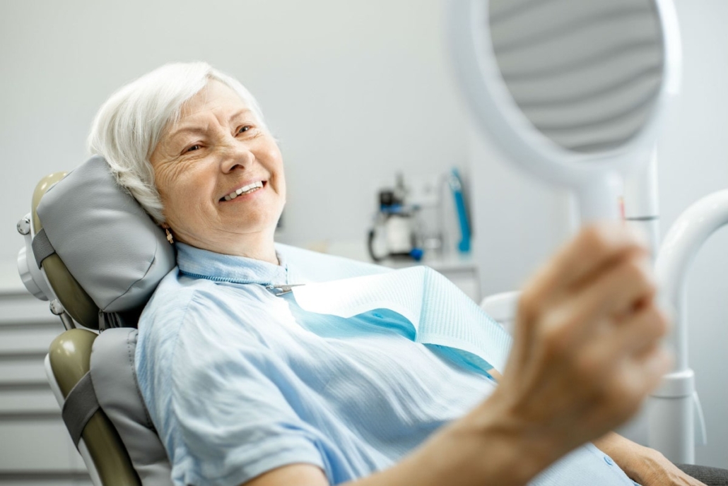 Elderly woman admiring her new dentures with a handheld mirror